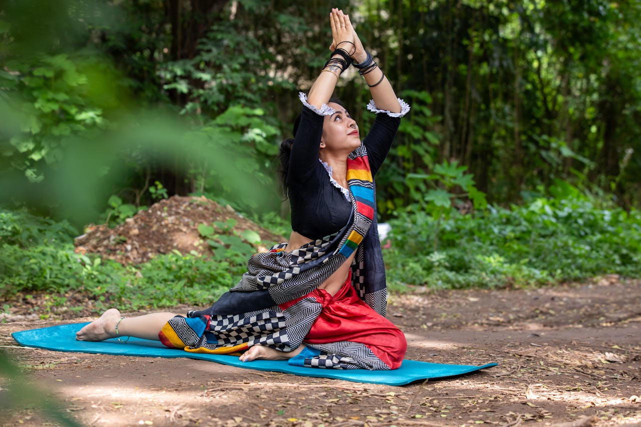 about-01 Woman practicing yoga pose outdoors in vibrant traditional attire, surrounded by lush greenery.